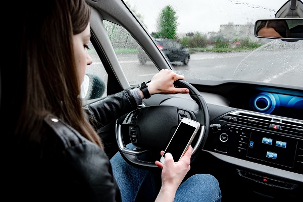 Young woman using mobile phone while driving car on bad weather condition.