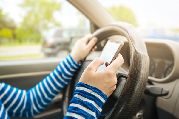 Woman driving car and texting message on smartphone